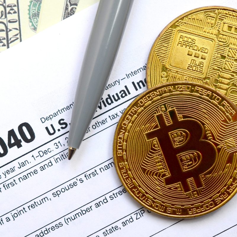 The pen, bitcoins and dollar bills is lies on the tax form 1040 U.S. Individual Income Tax Return. The time to pay taxes